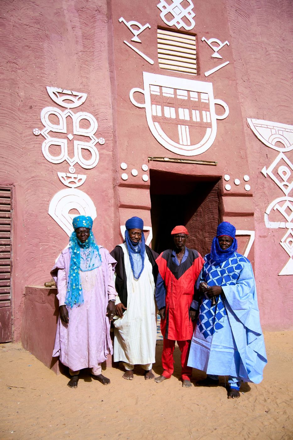 Personnes en tenue traditionnelle devant une maison de terre décorée